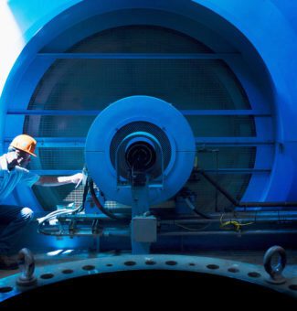 A male worker in a hard hat performs maintenance work at a hydroelectric power station.