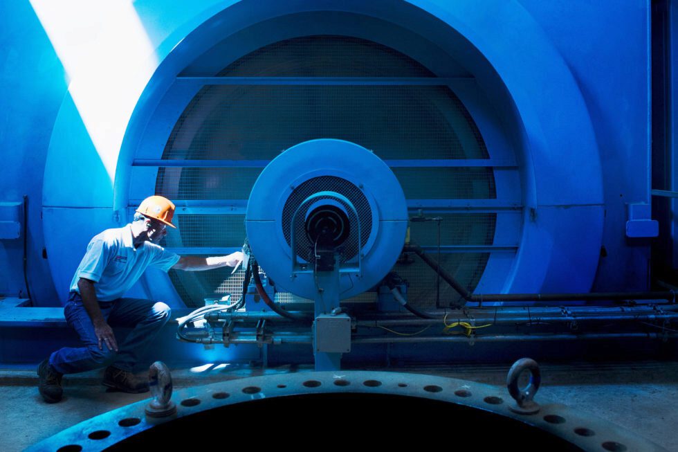 A male worker in a hard hat performs maintenance work at a hydroelectric power station.