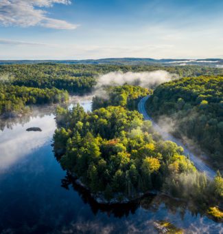 Aerial view of a country highway by a lake and through a forest on a misty morning