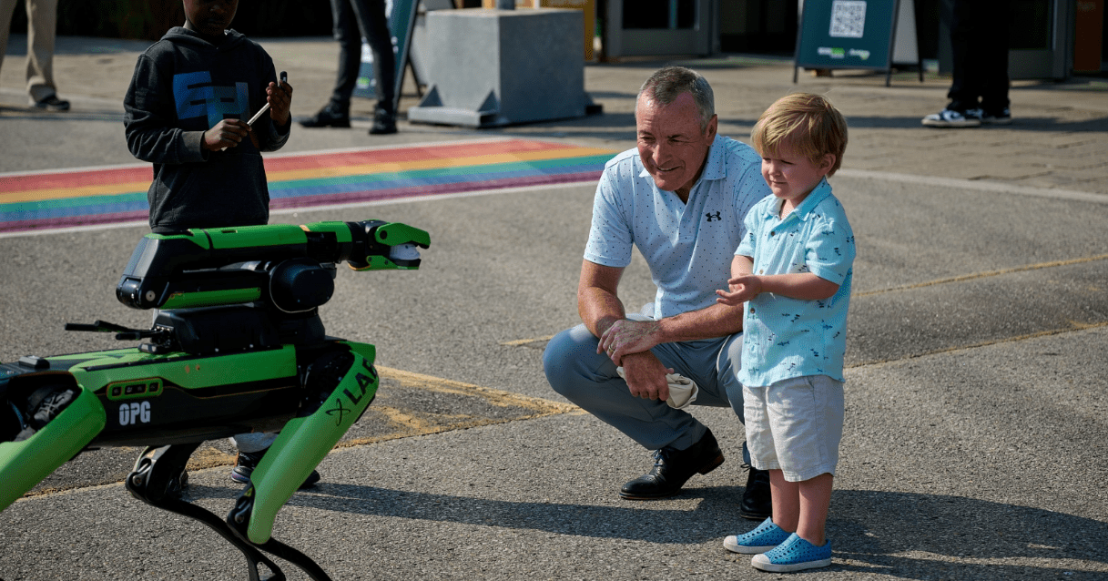 President & CEO, Ken Hartwick, and a child examine Spot; a robotic dog.