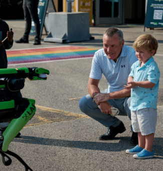 President & CEO, Ken Hartwick, and a child examine Spot; a robotic dog.