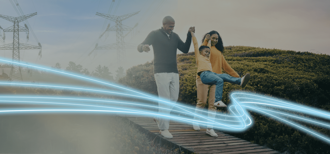 A family of three walk along a boardwalk with power transmission lines in the background.