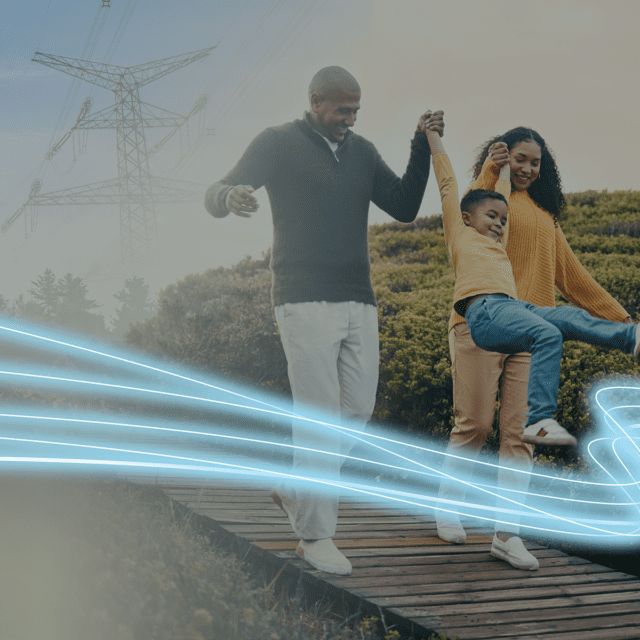 A family of three walk along a boardwalk with power transmission lines in the background.